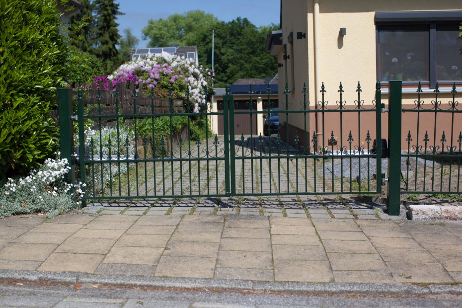 Zweiflügeliges Einfahrtstor aus Metall in Grün mit Zierspitzen vor einer Hofeinfahrt